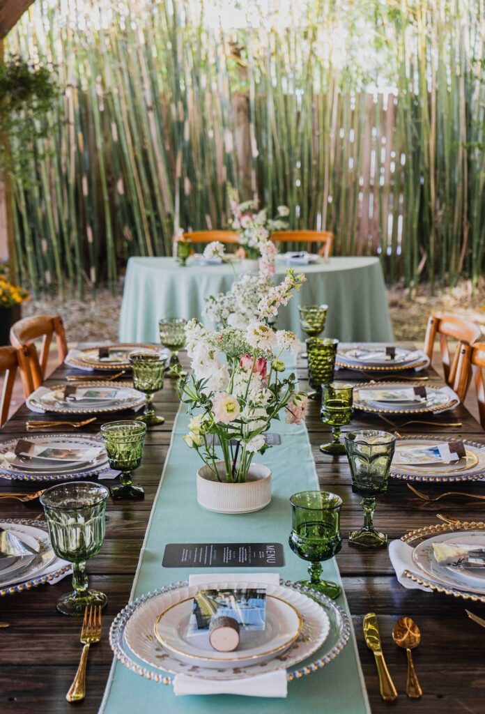 A long table with a sage runner, green glassware and a garden centerpiece